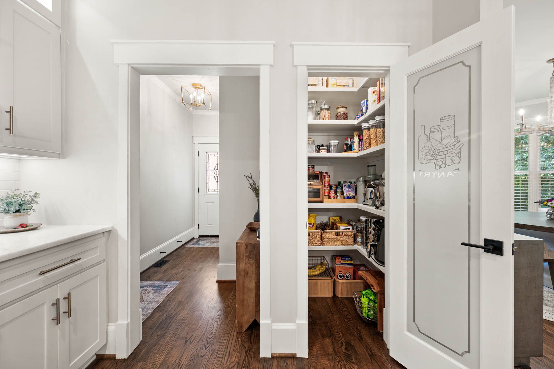 A kitchen with an open pantry featuring shelves filled with food items and a frosted glass door.  A hallway is visible in the background.