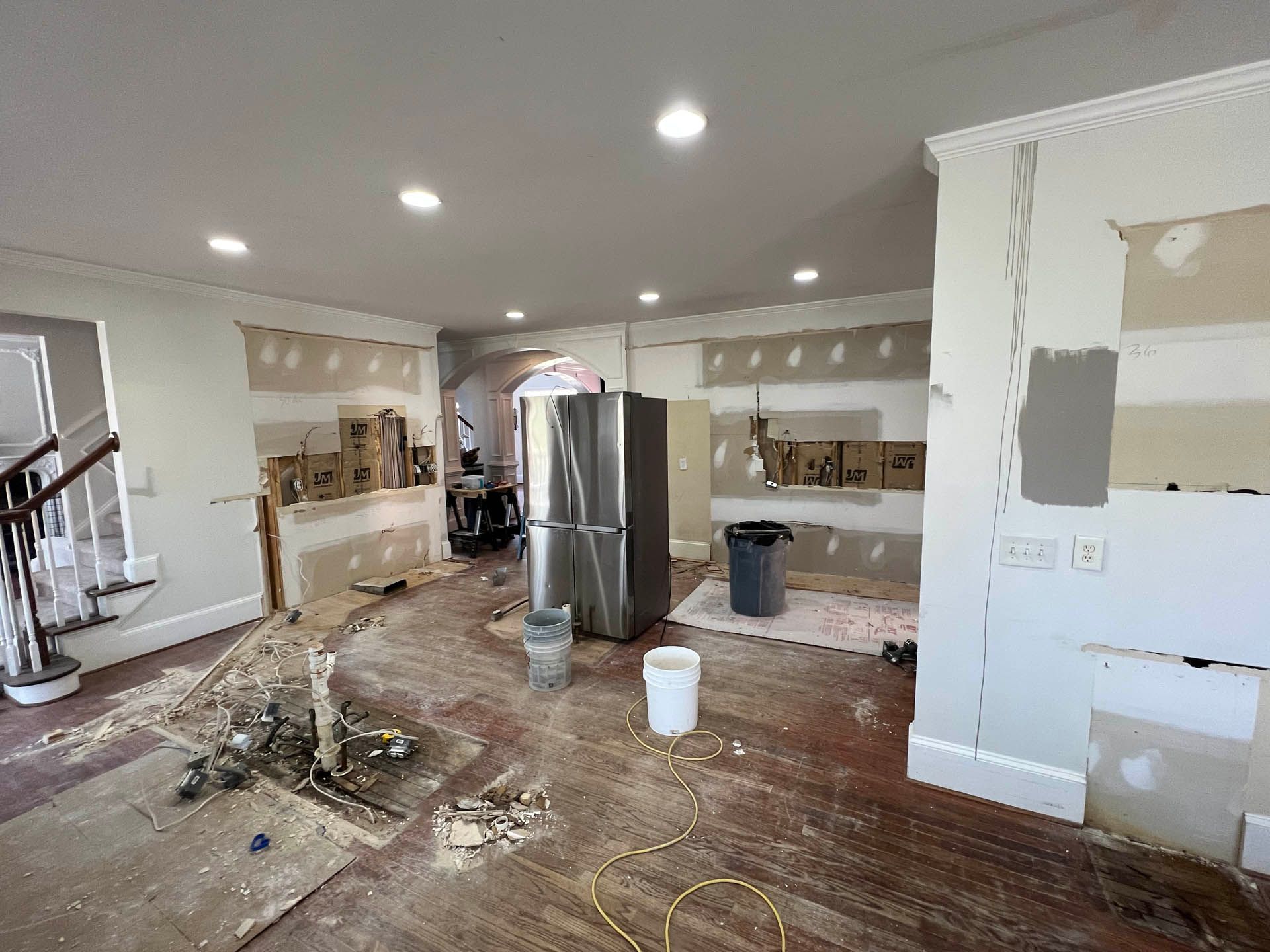 Room under renovation, with exposed walls, a refrigerator, and debris on the floor.