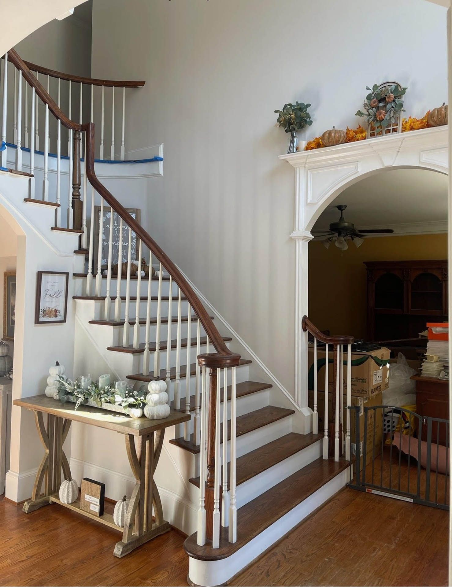 Wooden staircase with white balusters and brown handrails, leading up to a landing. A wooden table with decor sits beneath the stairs.
