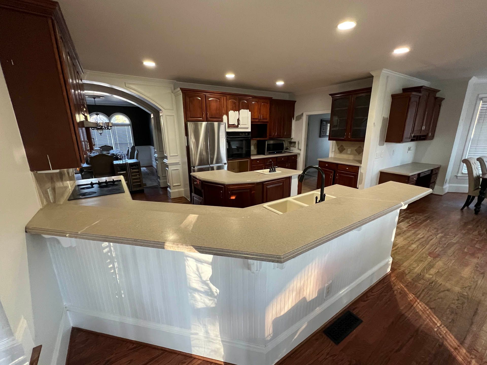 Kitchen with dark wood cabinets, stainless steel appliances, and a white countertop island with beadboard. The kitchen opens to a dining area.