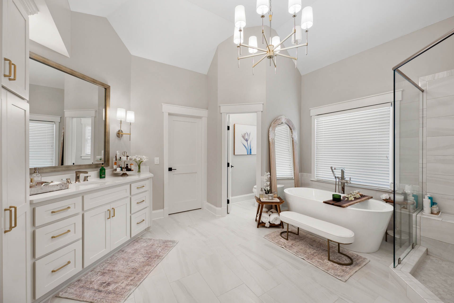 A luxurious white bathroom featuring a freestanding tub, double vanity, and a glass shower. Soft pink accents and gold fixtures.