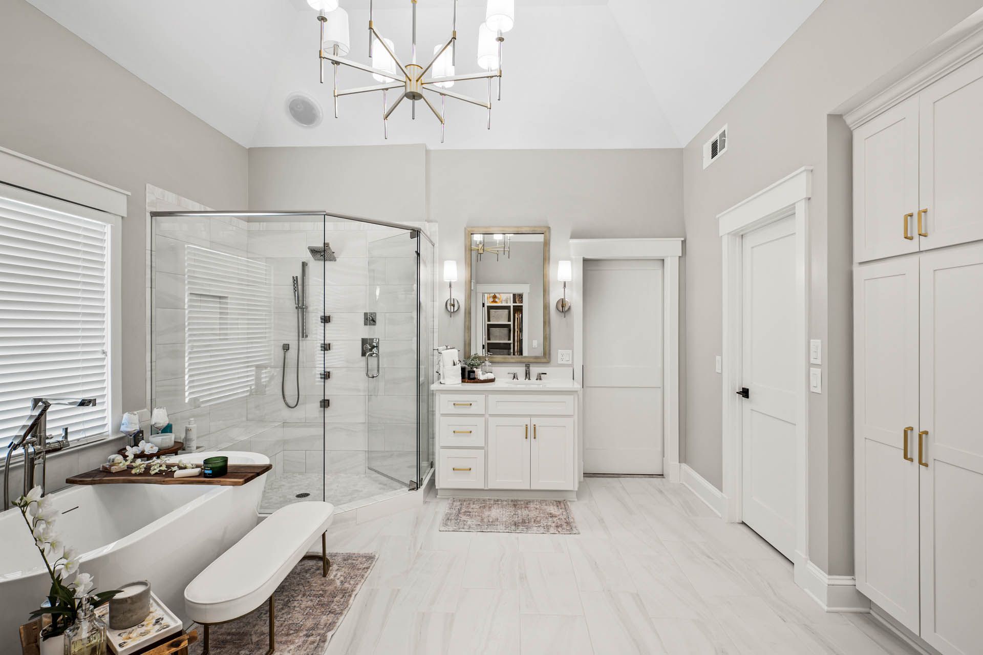 Spacious, bright bathroom with a glass shower, freestanding tub, white cabinetry, and a modern chandelier.