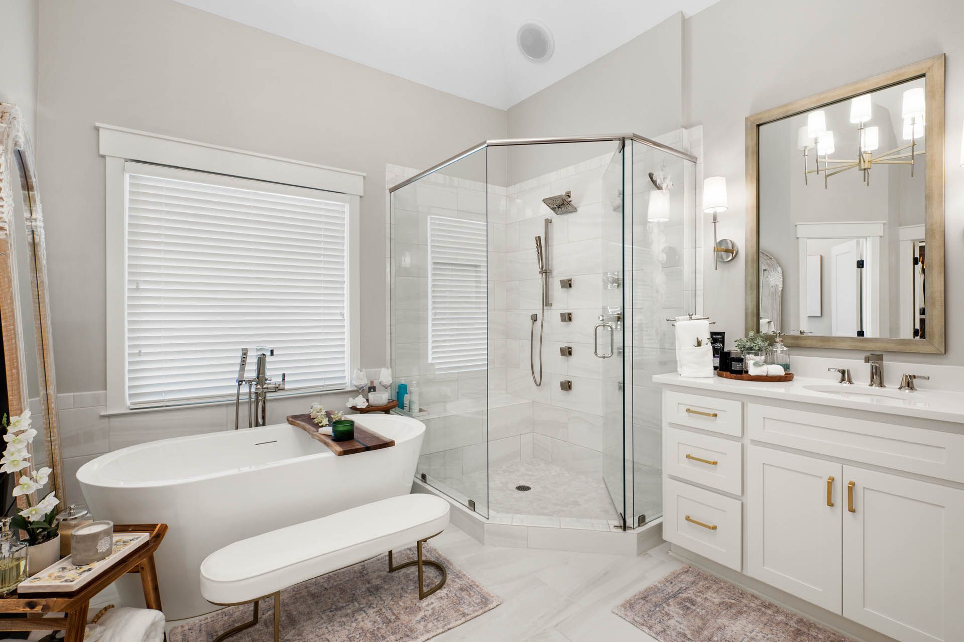 Luxurious white bathroom with a standalone tub, glass shower, white vanity, and gold accents.