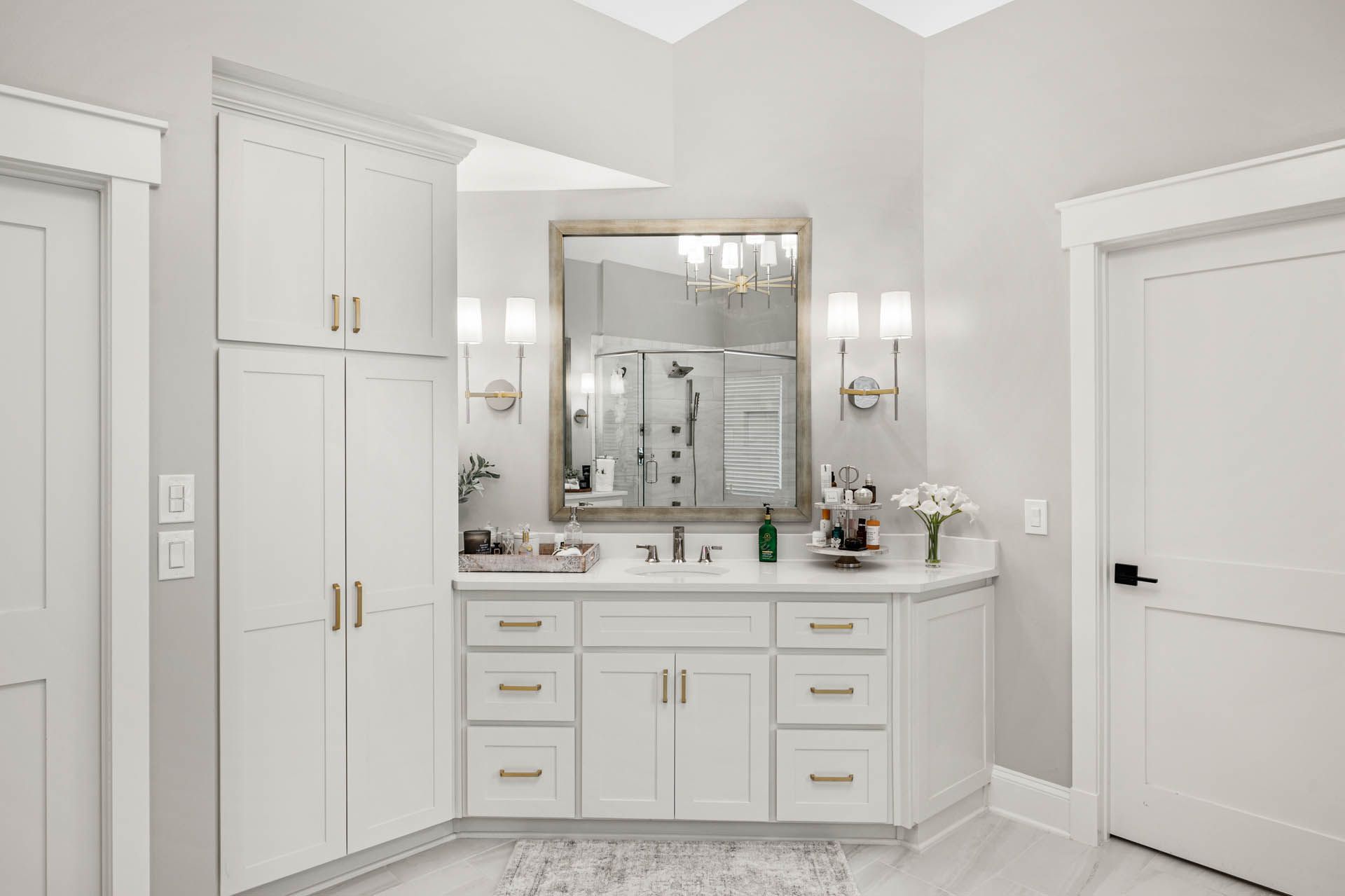 White bathroom with a vanity, large mirror, and cabinets. The space has a clean, modern design with gold hardware accents.
