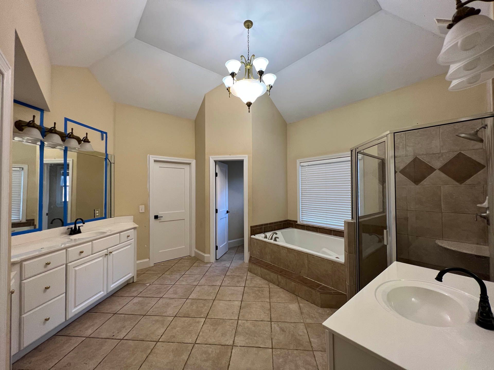 Spacious bathroom with white vanities, a jacuzzi tub, and a walk-in shower. Light tan walls and tile floors.