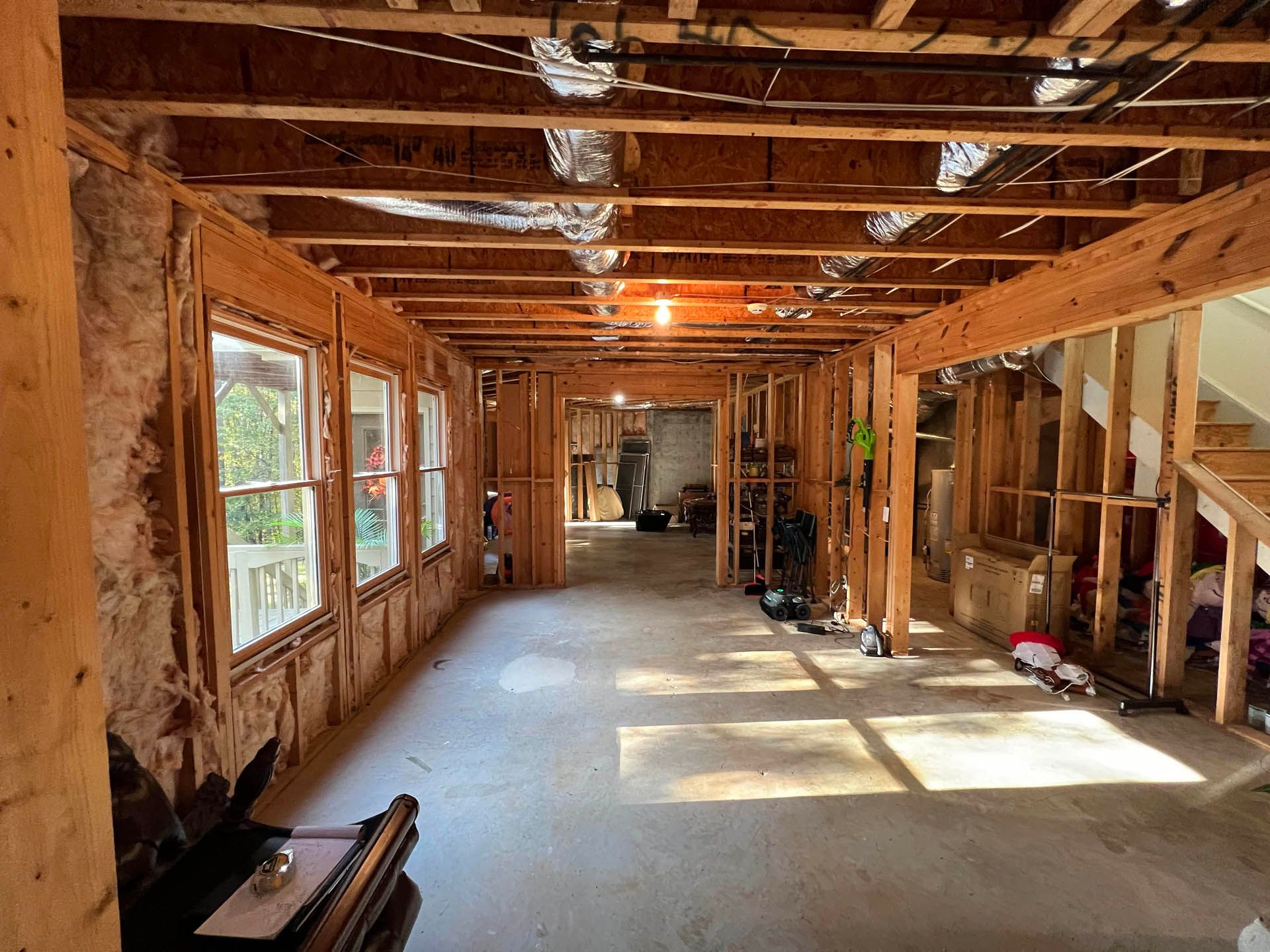Interior view of a room under construction. Exposed wooden framing, concrete floor, and multiple windows on the left side.