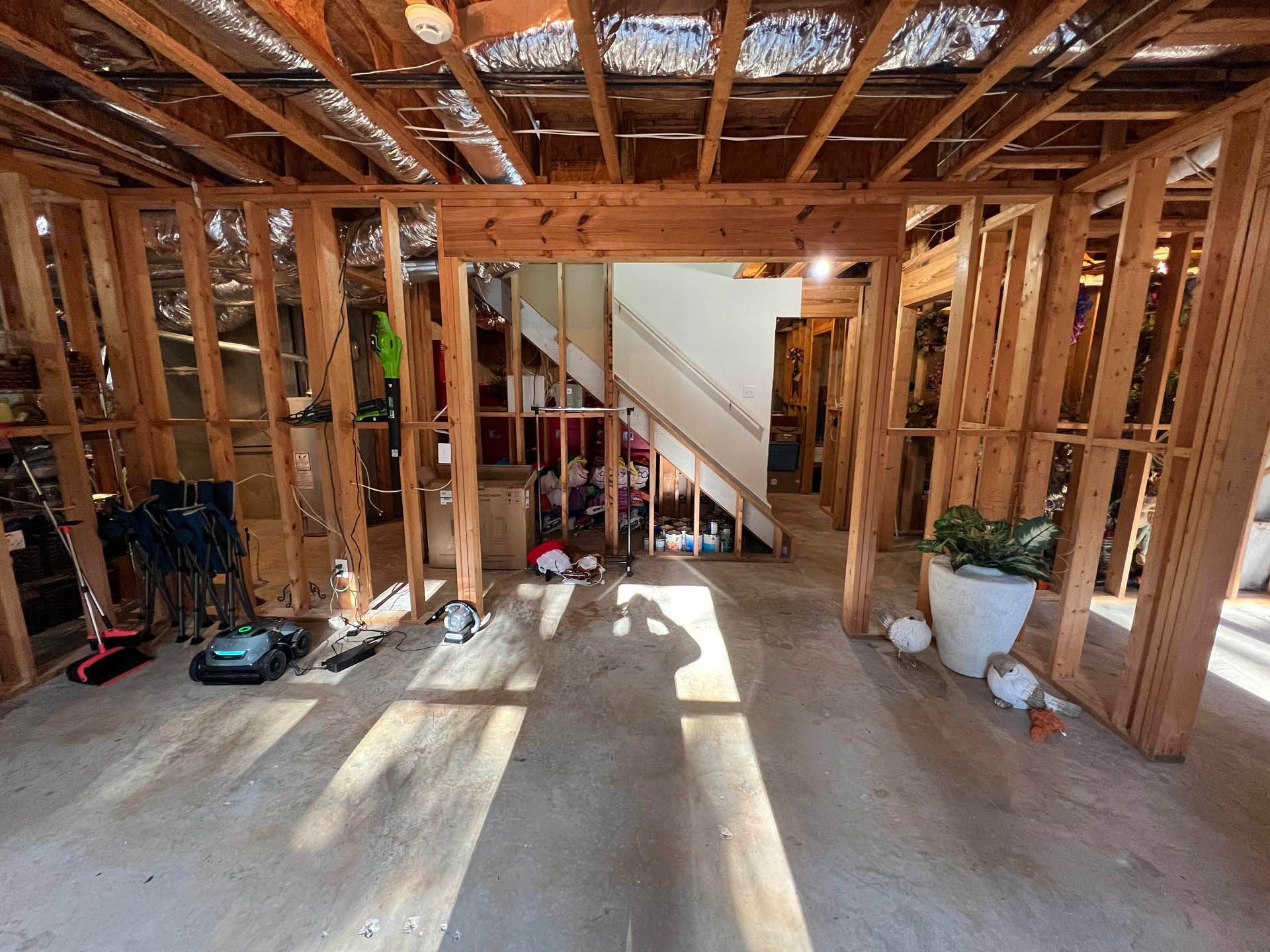 Interior view of a room under construction, showing exposed wooden beams and framing. Sunlight streams through the open spaces.