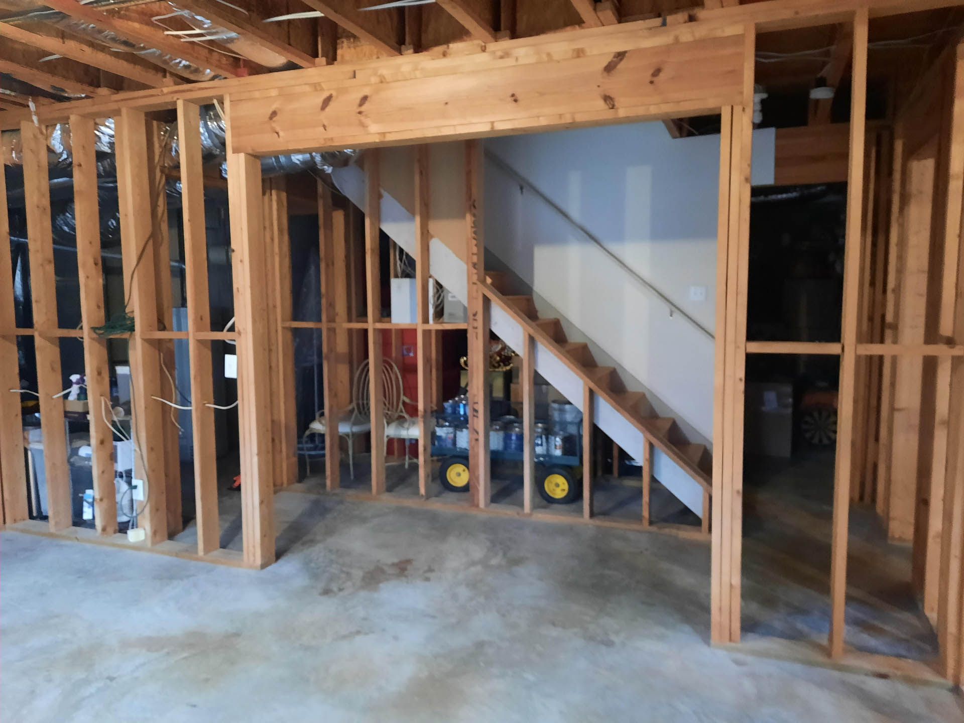 Unfinished basement with wooden framing around a stairwell. The stairs lead upward; yellow toy tractors are visible.