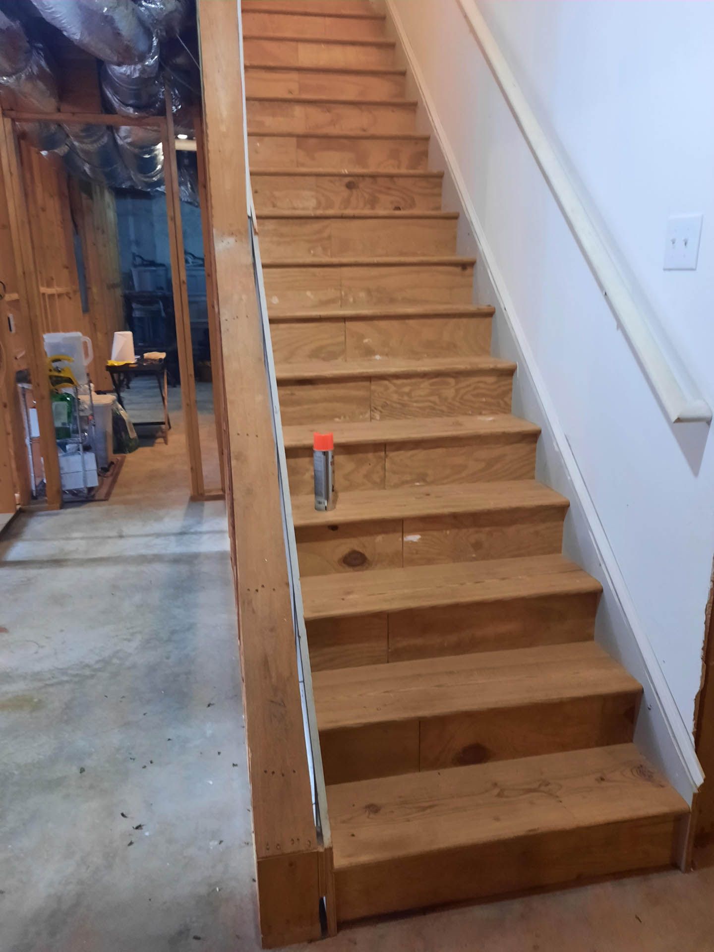 Wooden staircase leading upwards from a concrete floor. Handrail on one side, open space on the other.
