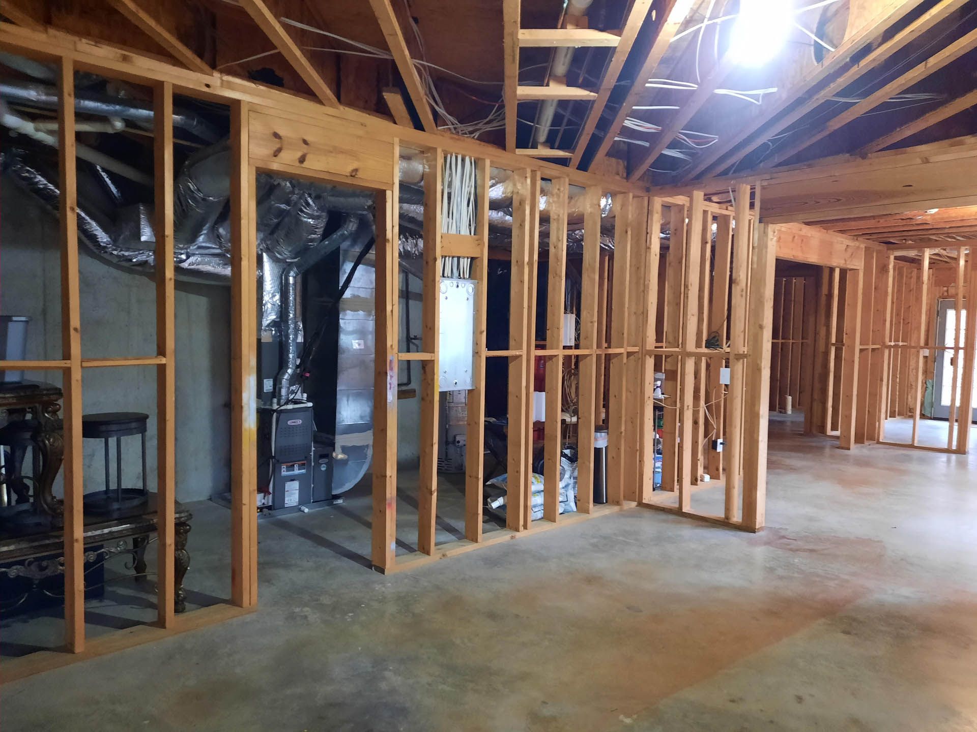 Interior view of a basement with wooden wall framing, revealing unfinished walls and a concrete floor. Includes HVAC system and ductwork.