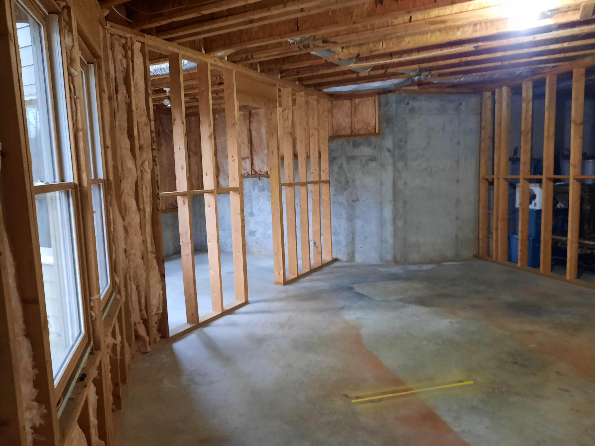 Interior view of a room under construction with exposed wooden framing, insulation, and a concrete floor and walls.