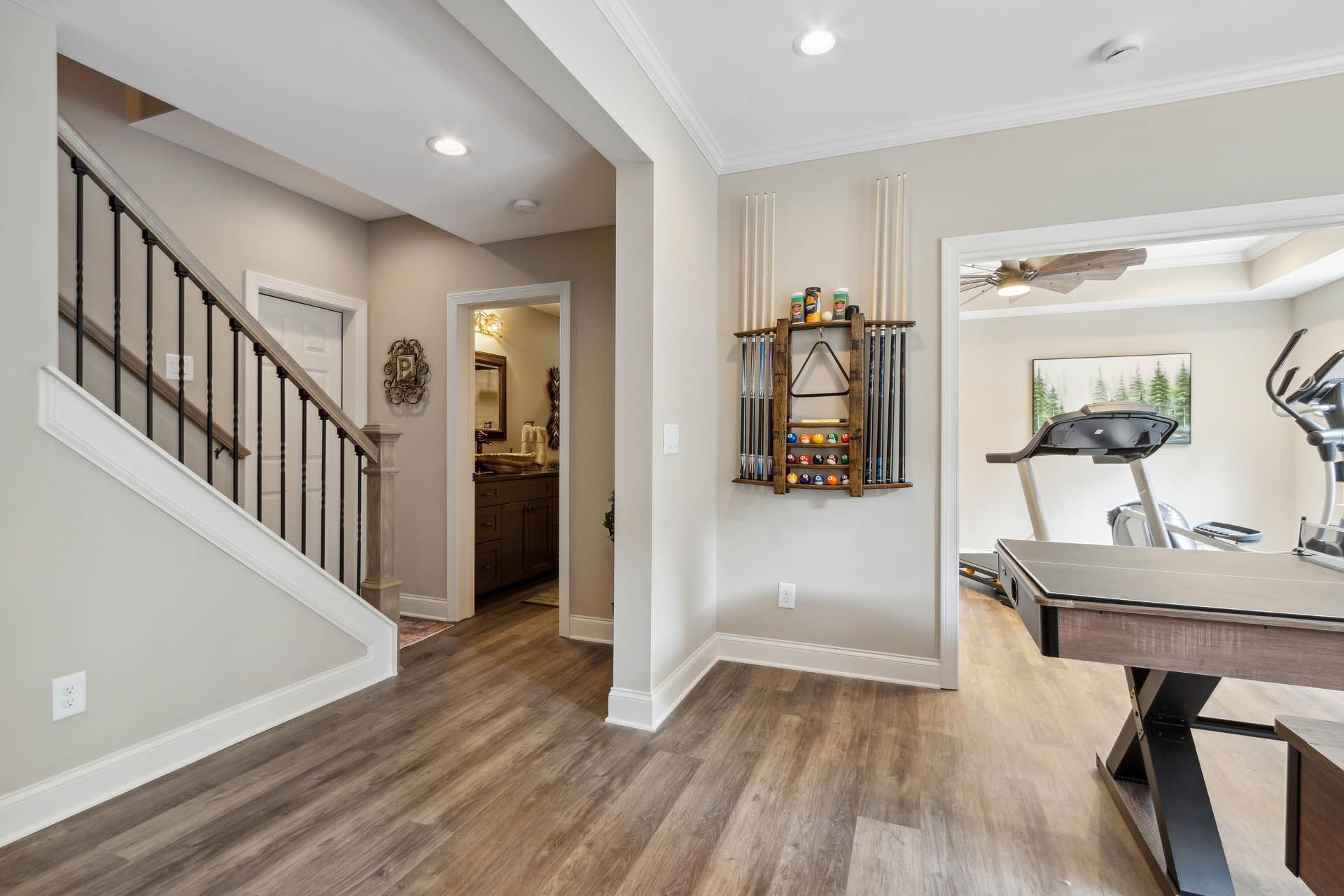 Interior view: Entryway with staircase, bathroom, and home gym. Light wood flooring, neutral walls, and a pool cue rack.