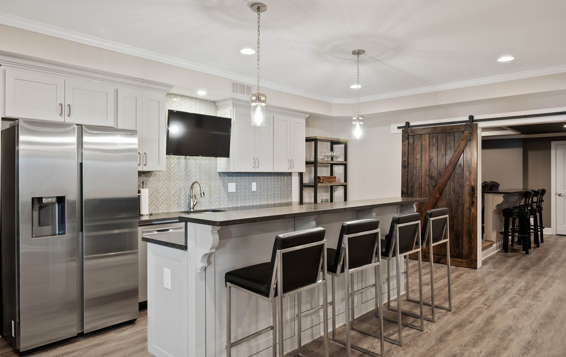 Modern kitchen with a stainless steel fridge, breakfast bar, and a barn door entrance.
