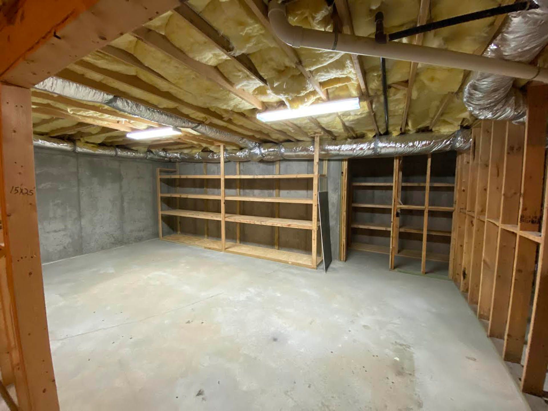 Empty basement with concrete floor, exposed framing, shelving units, and insulated ceiling.