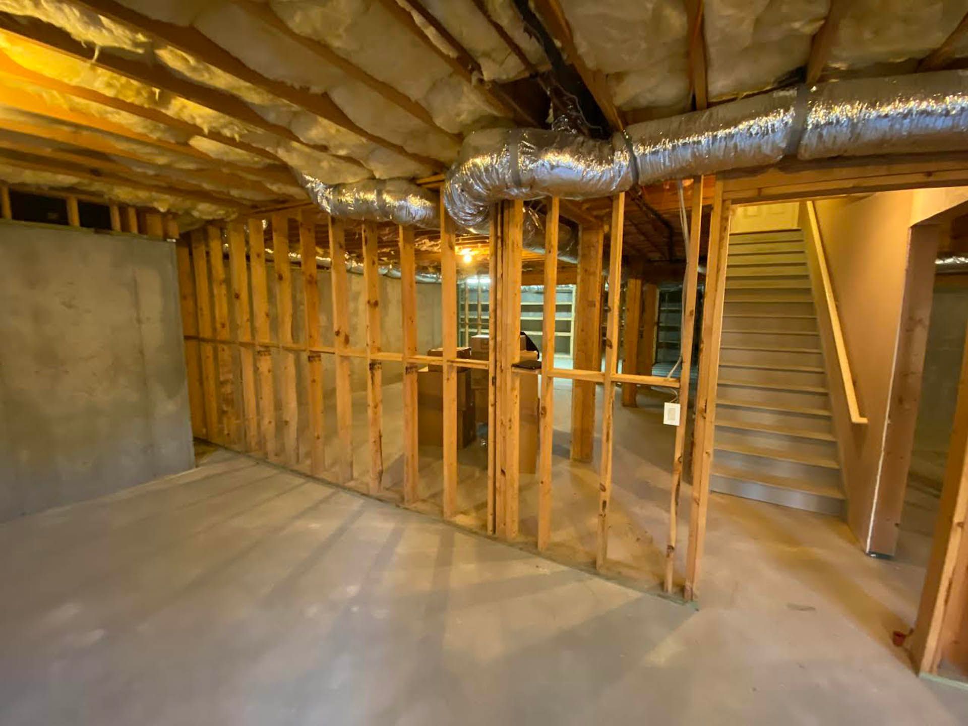 Basement framing with exposed wooden studs, ductwork, and stairs. Concrete floor and insulation visible in the ceiling.