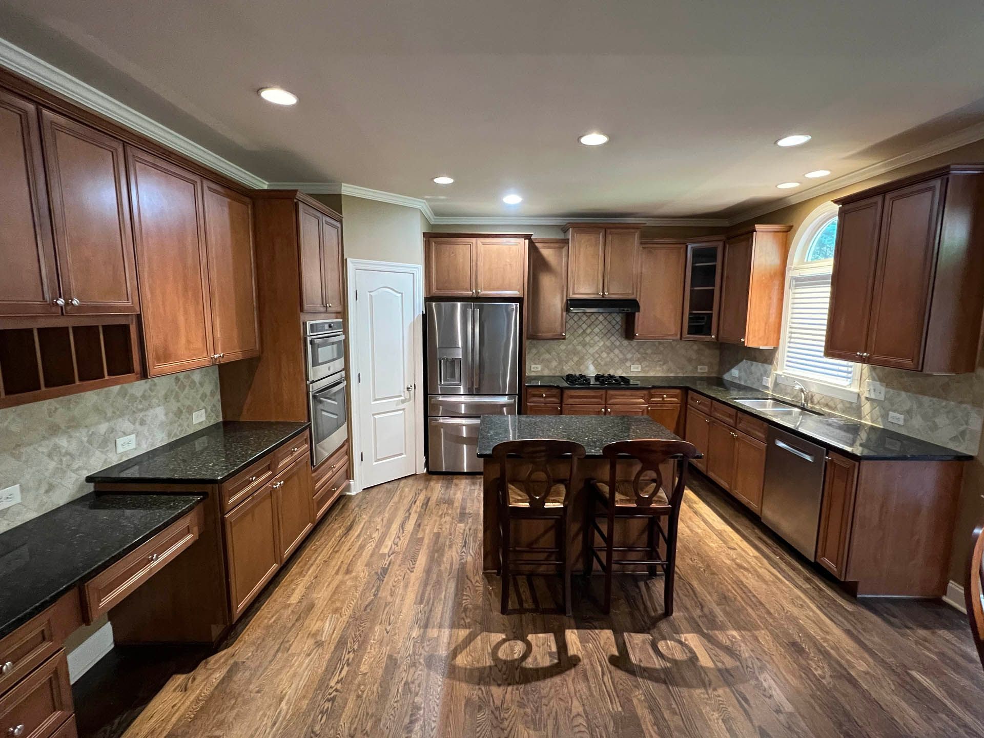 Spacious kitchen with brown cabinets, black countertops, stainless steel appliances, and a central island with two bar stools.