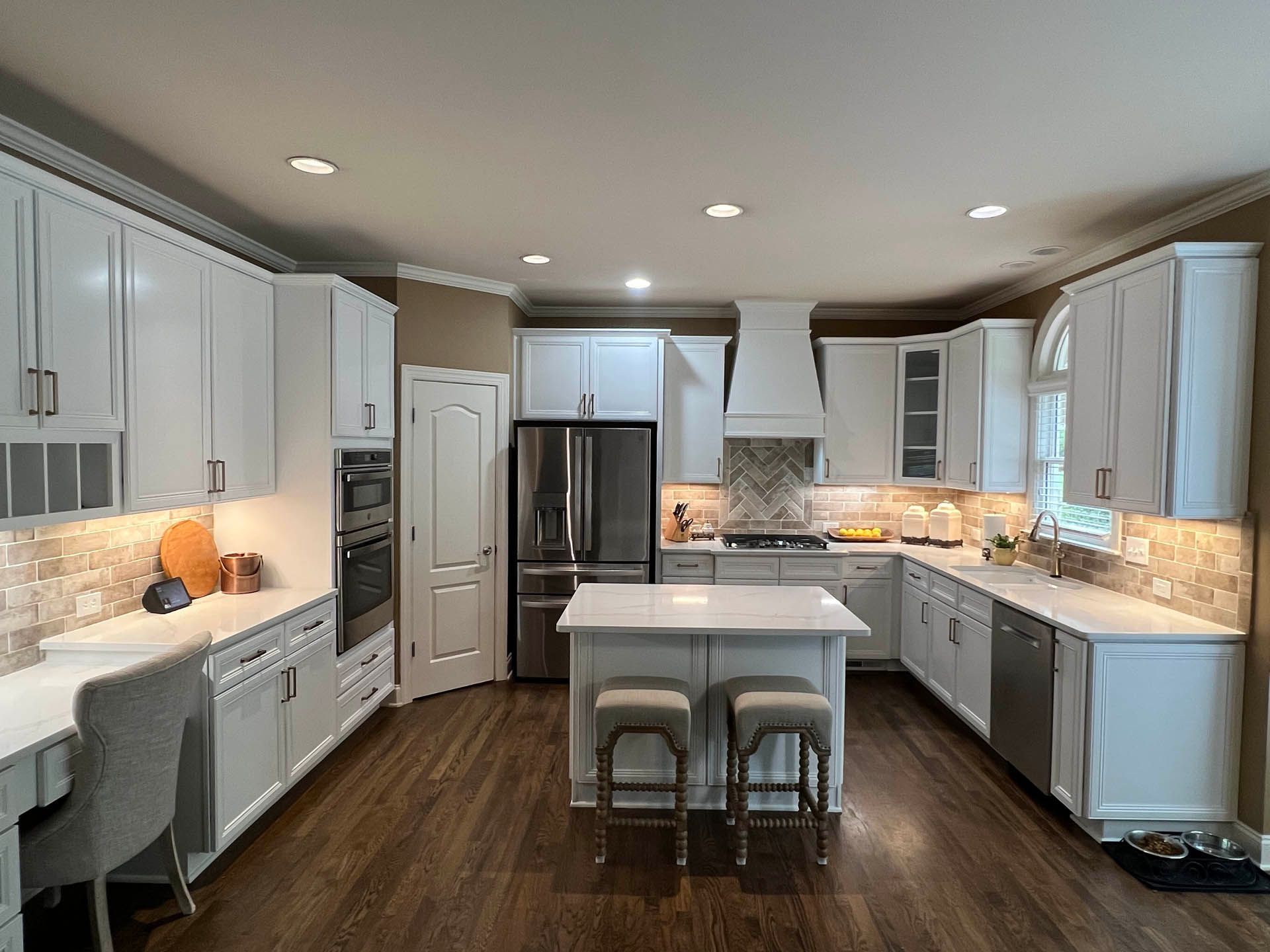 A bright white kitchen with a central island, white cabinets, stainless steel appliances, and wooden floors.