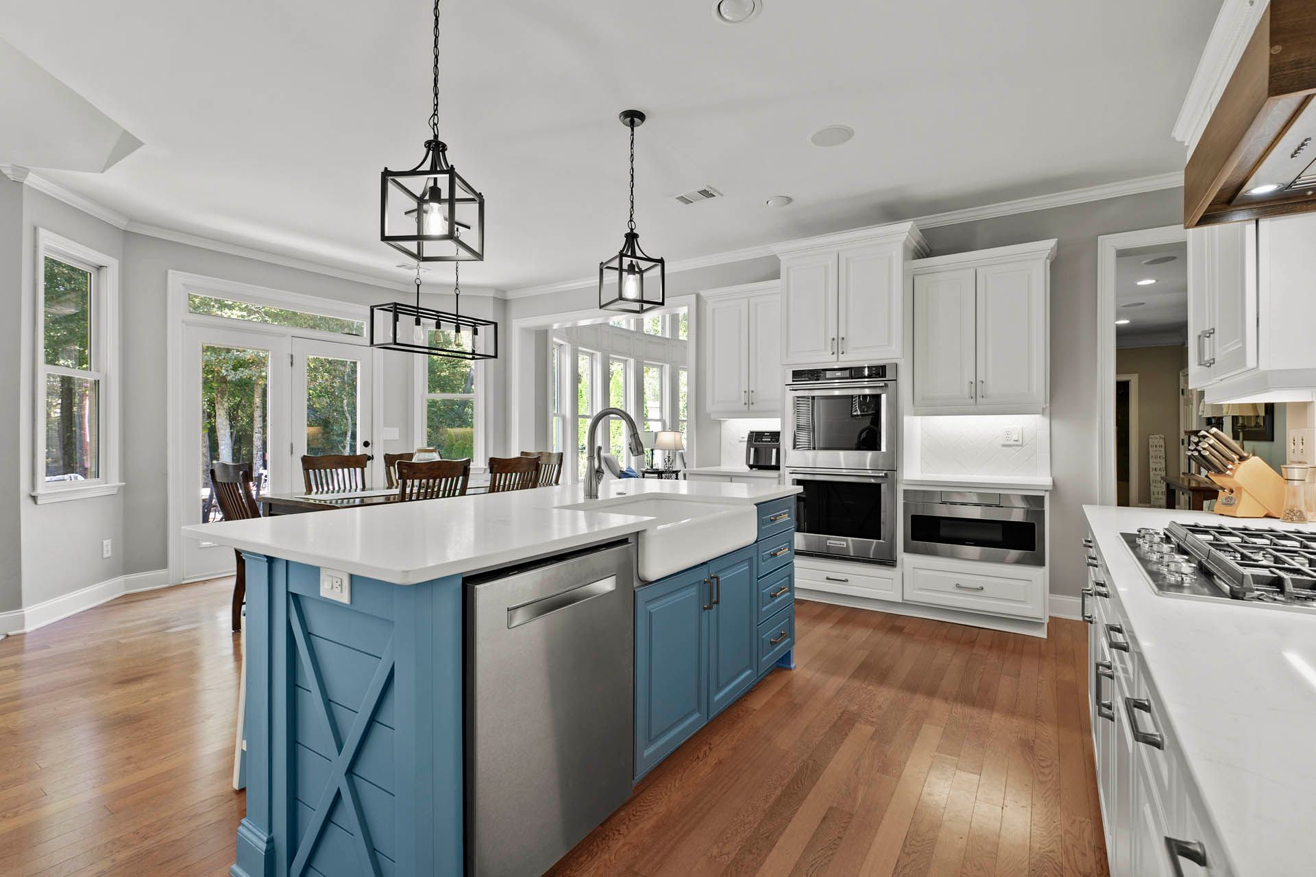 Spacious kitchen with a blue island, stainless steel appliances, white countertops, and hardwood floors.