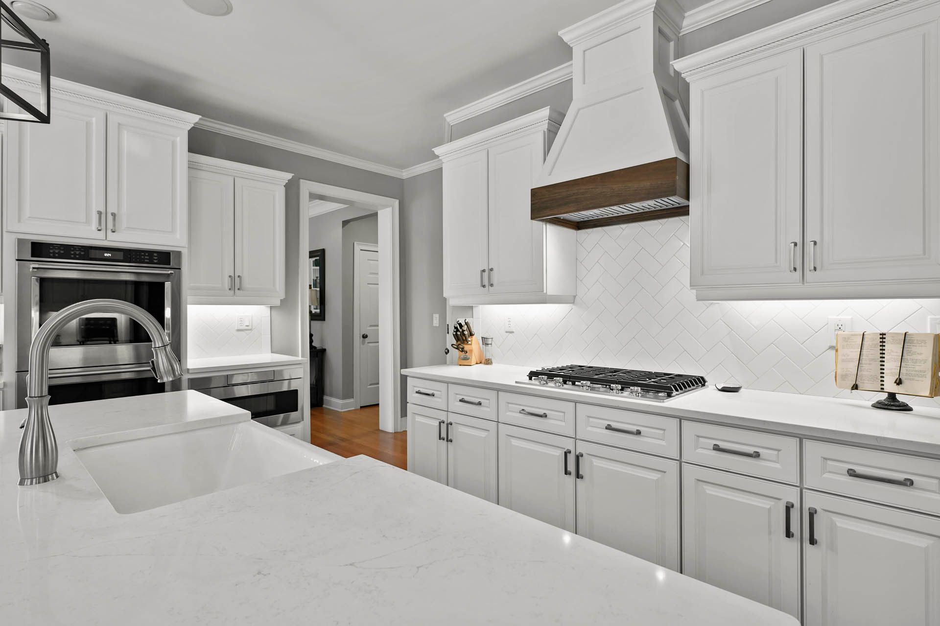 White kitchen with quartz countertops, cabinets, and backsplash, with a stainless steel oven, range, and faucet.