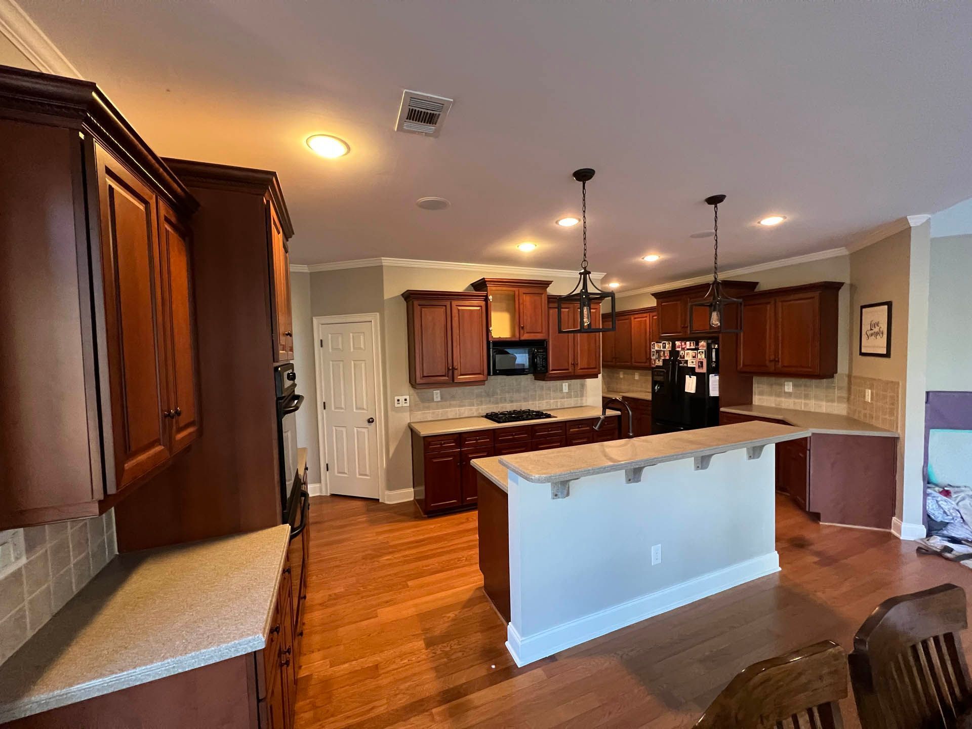 A kitchen with dark wood cabinets, light countertops, and hardwood floors. It includes an island with a light-colored base.