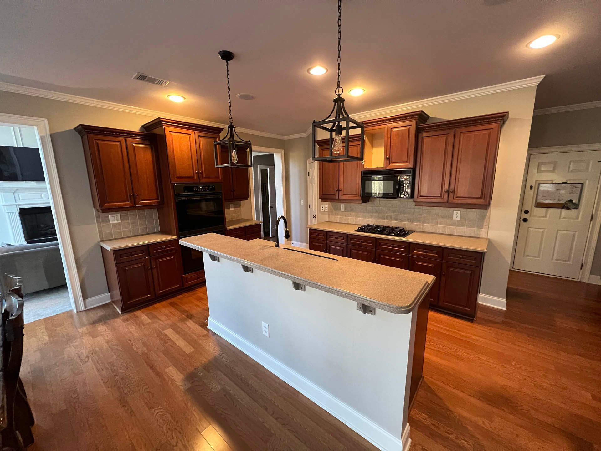 A kitchen with dark wooden cabinets, a central island, and hardwood floors.  Two decorative light fixtures hang above the island.