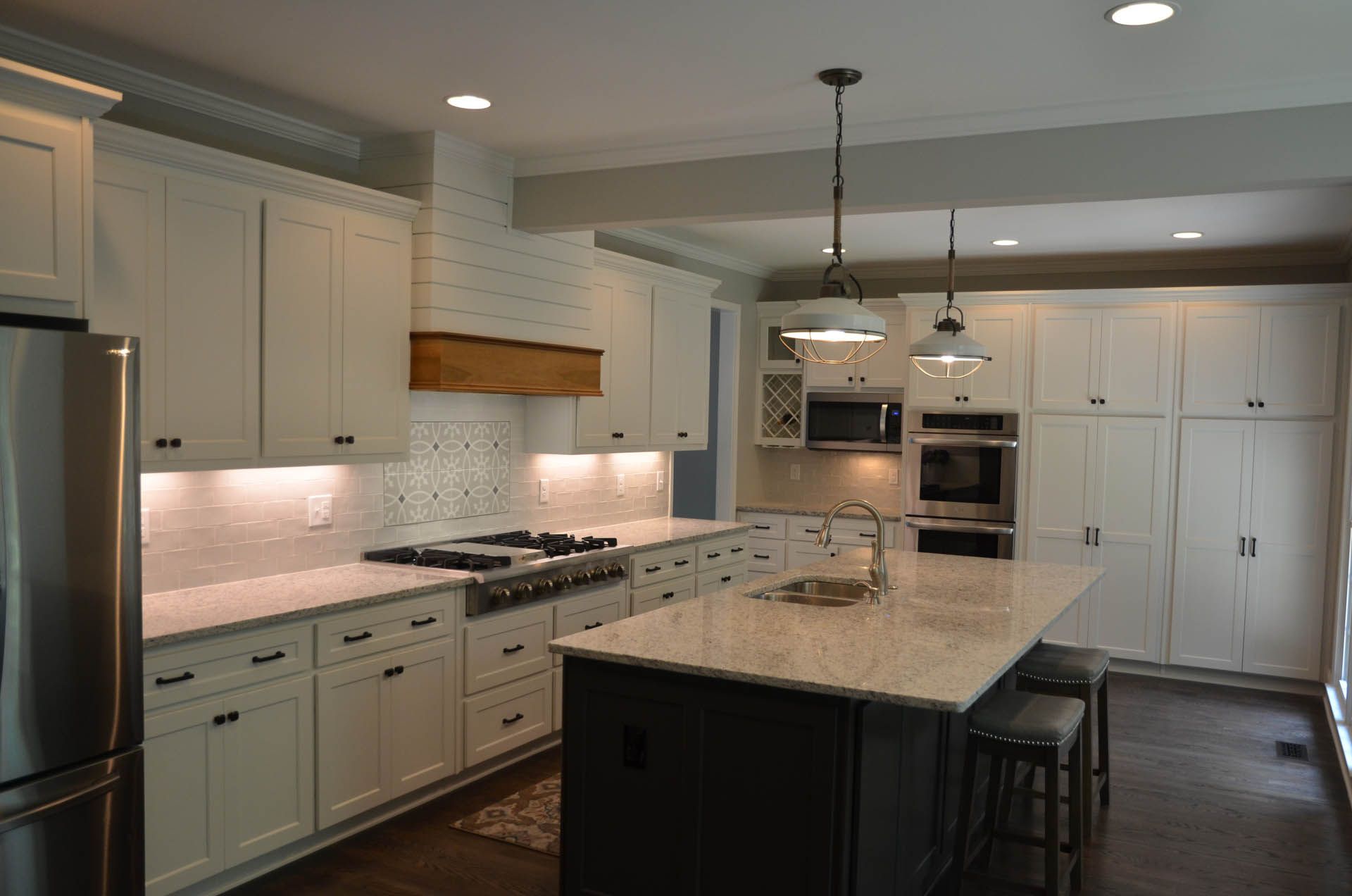 A modern kitchen with white cabinets, a dark island, and stainless steel appliances. Overhead lighting illuminates the space.