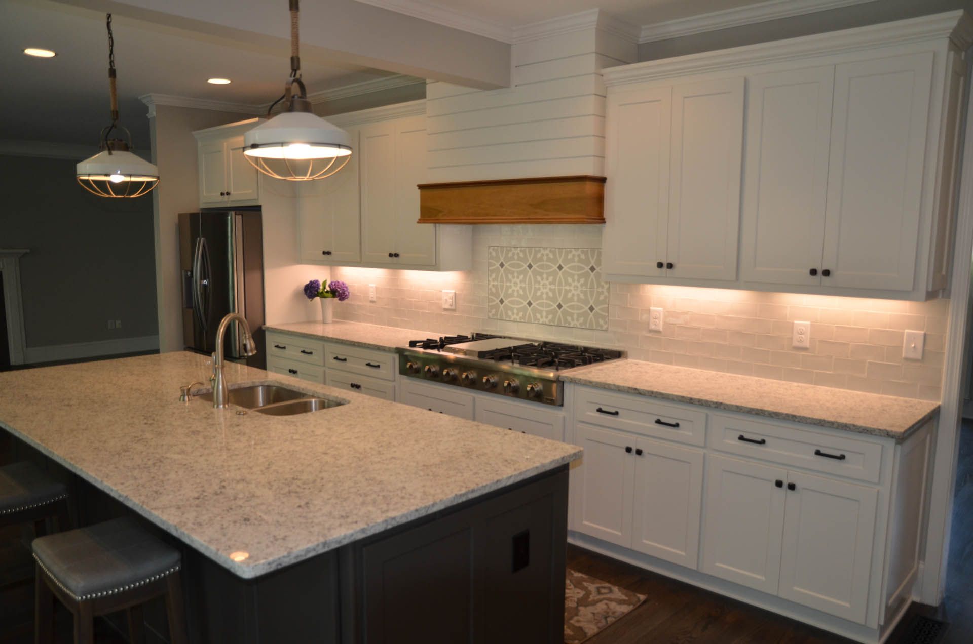 Modern white kitchen with a large island, light countertops, dark cabinets, and stainless steel appliances.