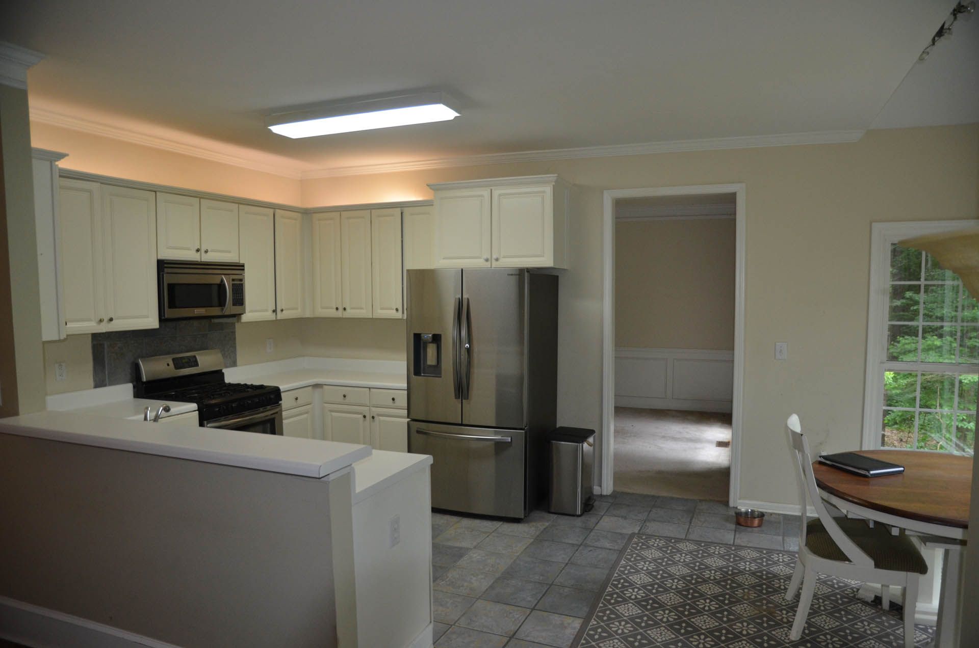 Kitchen with white cabinets, stainless steel appliances, and gray tile floor. A dining area is in the background.