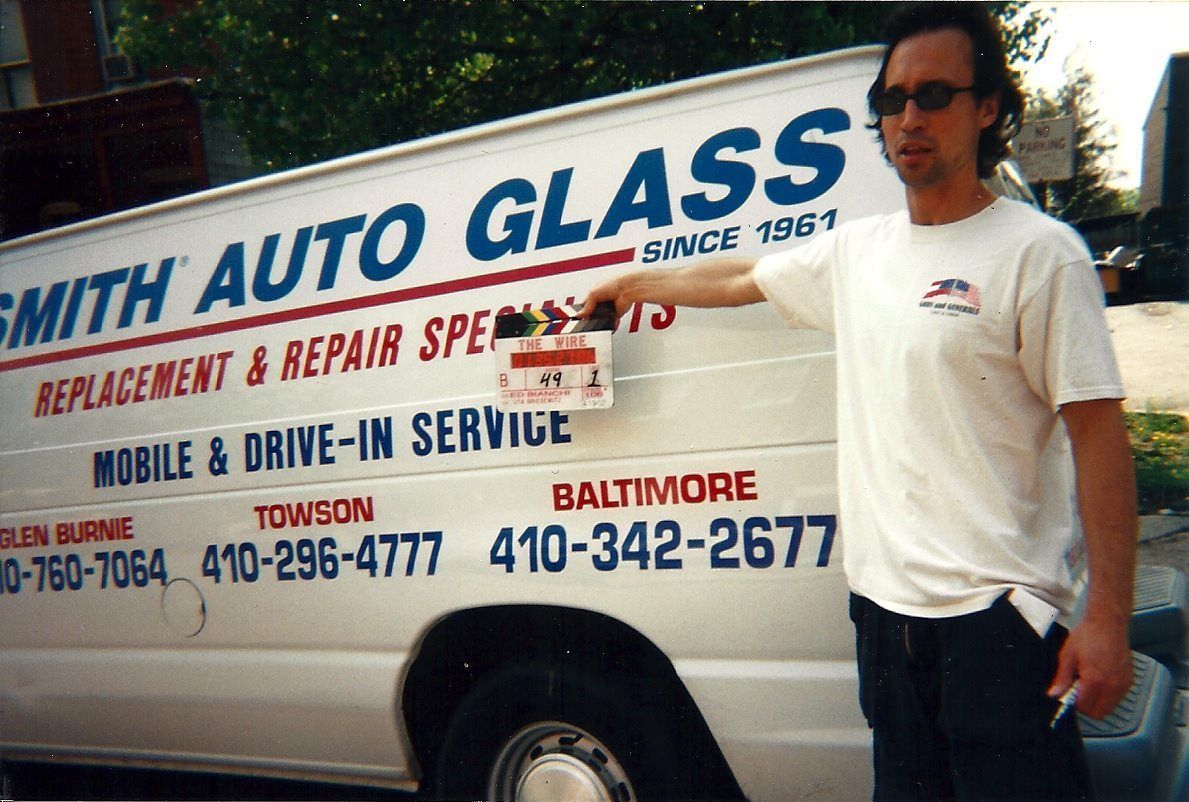 a film crew memeber holds a clap board in front of a smith auto glass van between takes during the filming of a movie