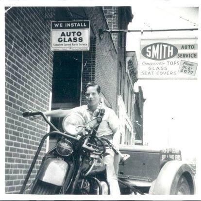 a vintage photo of a boy sitting on a motorcycle that was used for glass delivery