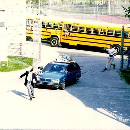 smith auto glass on the set of a movie. a blue car driving toward a man as a camera man films. the blue car had a windshield replaced by smith auto glass