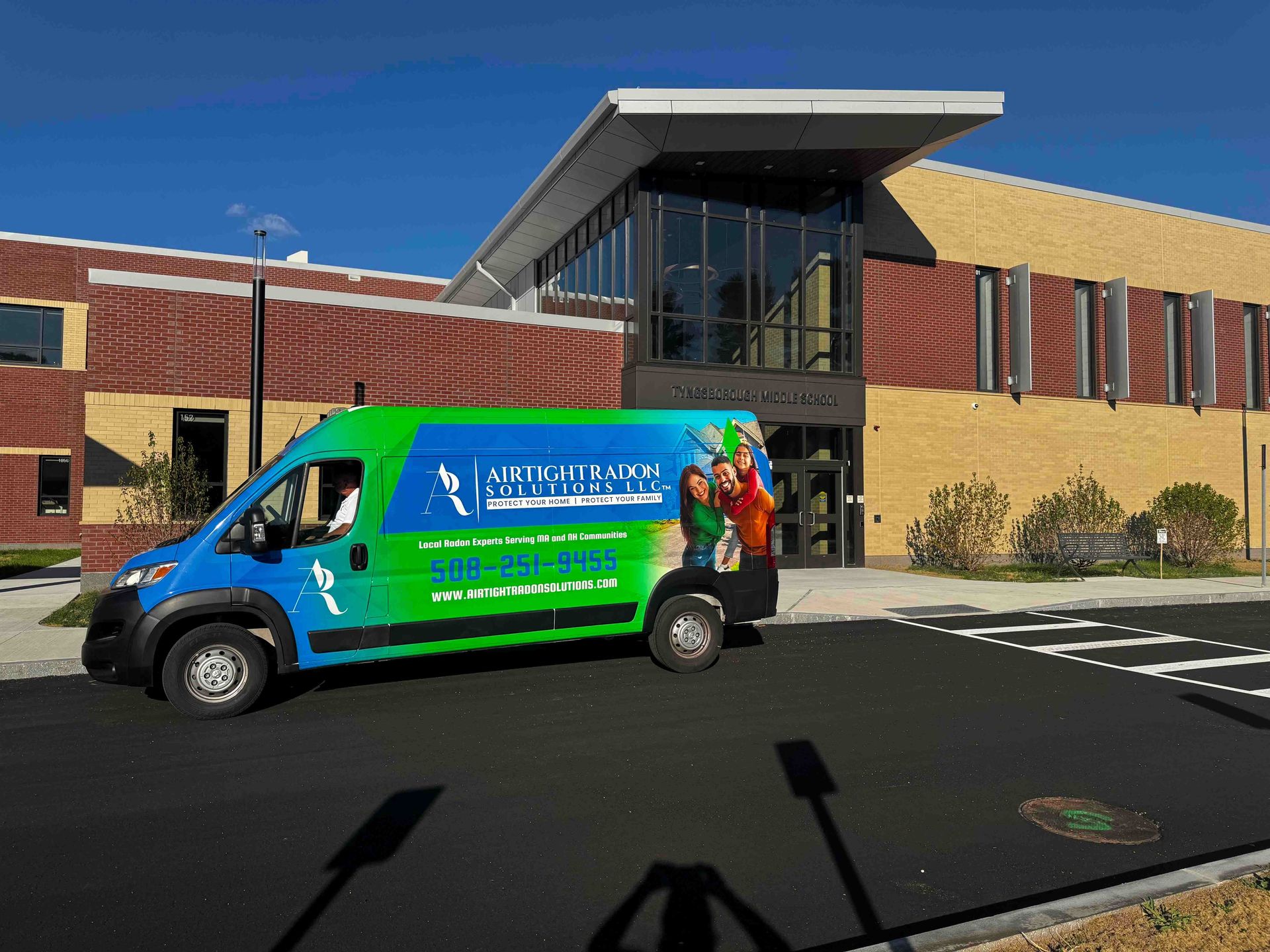 A blue and green van parked in front of a brick building with glass doors; sunny day.
