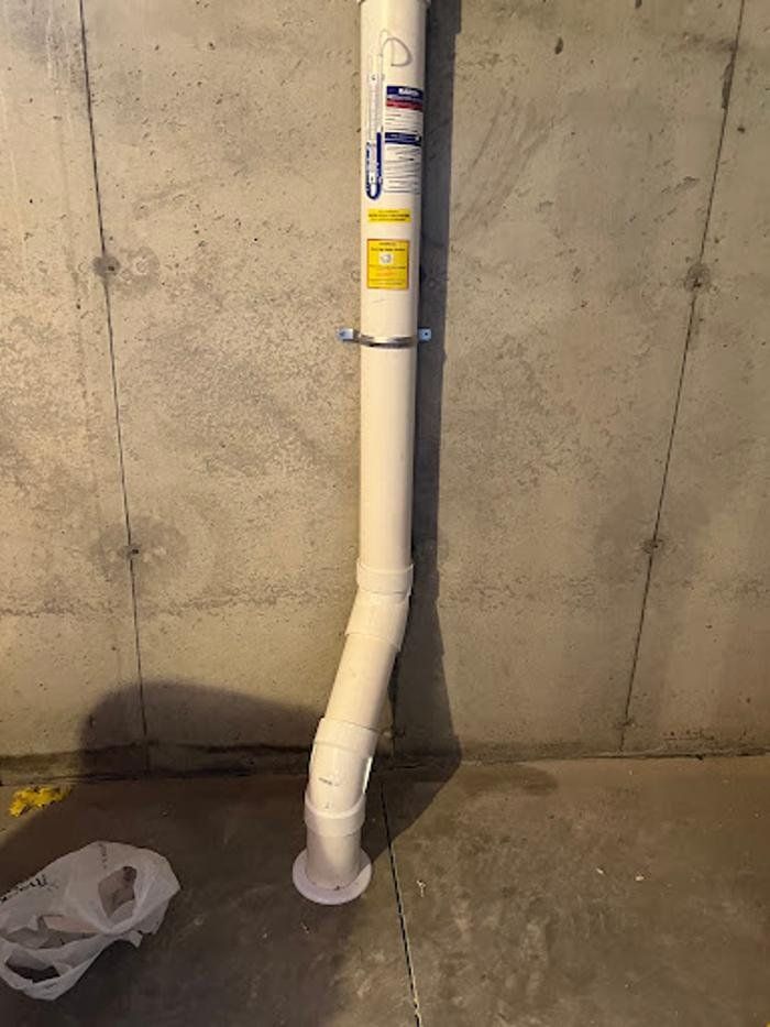 A white pipe is hanging from a concrete wall in a basement.