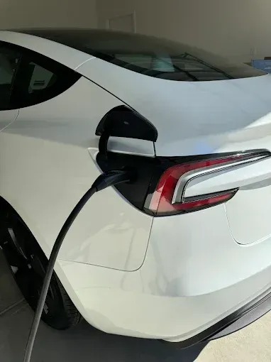 A white Tesla charging at home, with the charging cable plugged into the rear driver-side port.