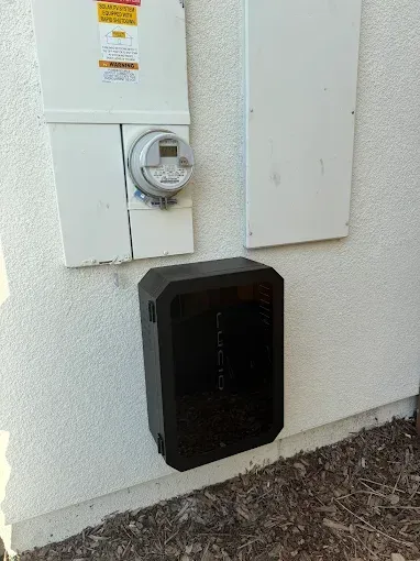 An electric meter and a black Lucid home charging station mounted on a white exterior wall.