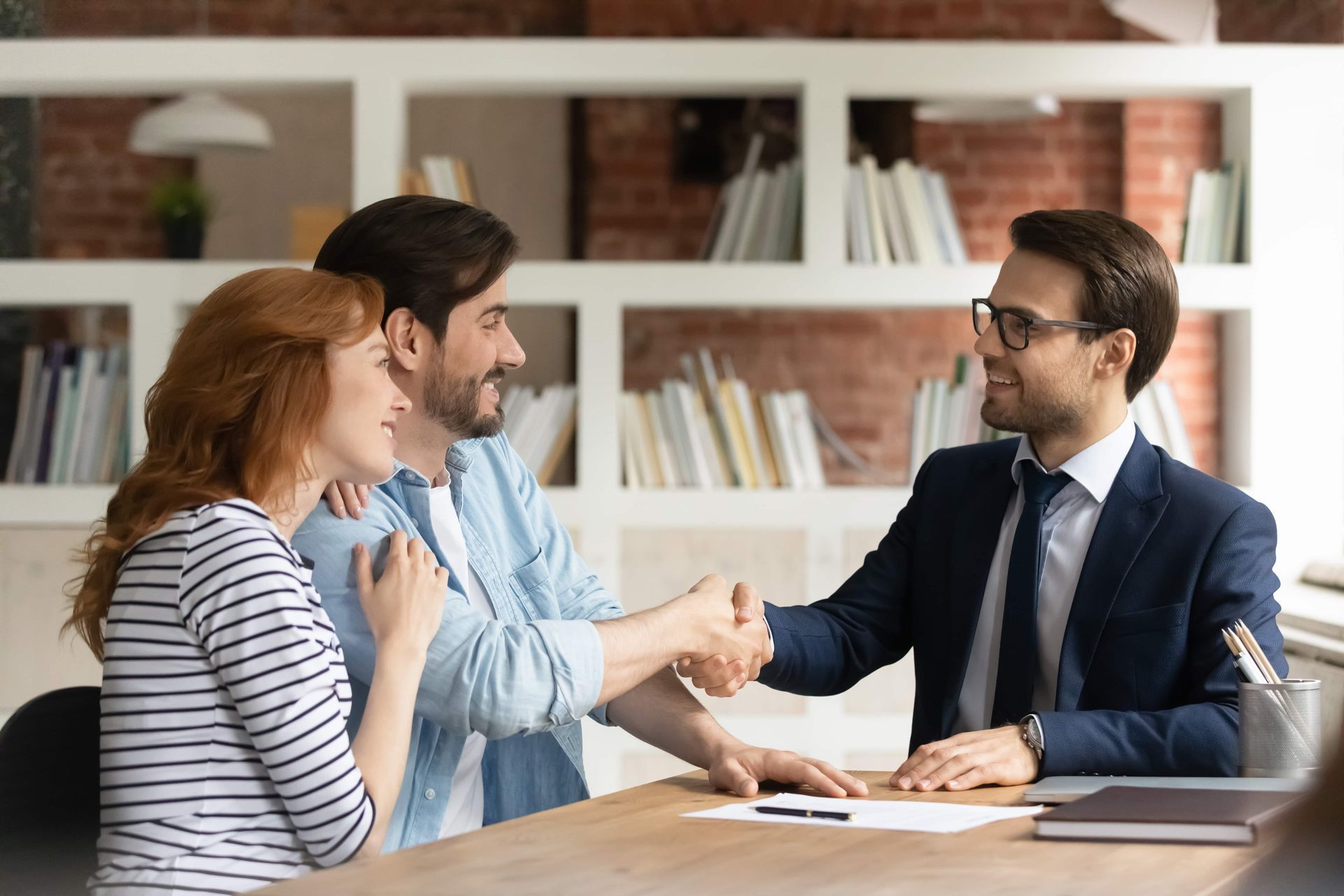 A couple shaking hands with a financial advisor at a desk in an office setting.