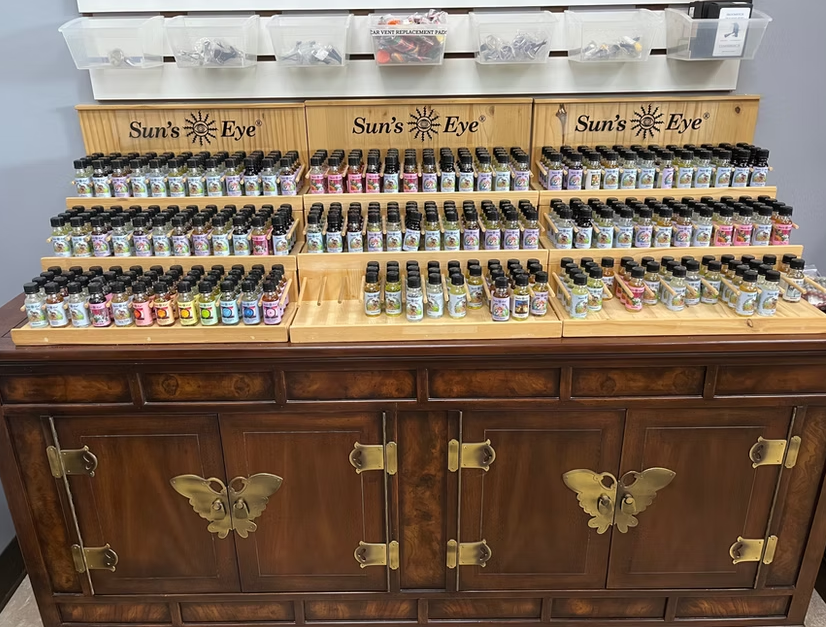A display of Sun's Eye essential oil bottles on a wooden cabinet. The bottles are in various colors and scents.