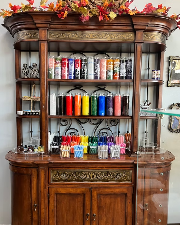 A wooden cabinet displays various colorful candles and tumblers. Autumn foliage decorates the top.