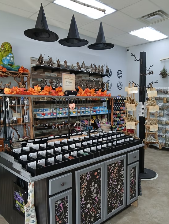 A craft store interior with a central display table, shelves, and Halloween decorations. Witch hats hang from the ceiling.
