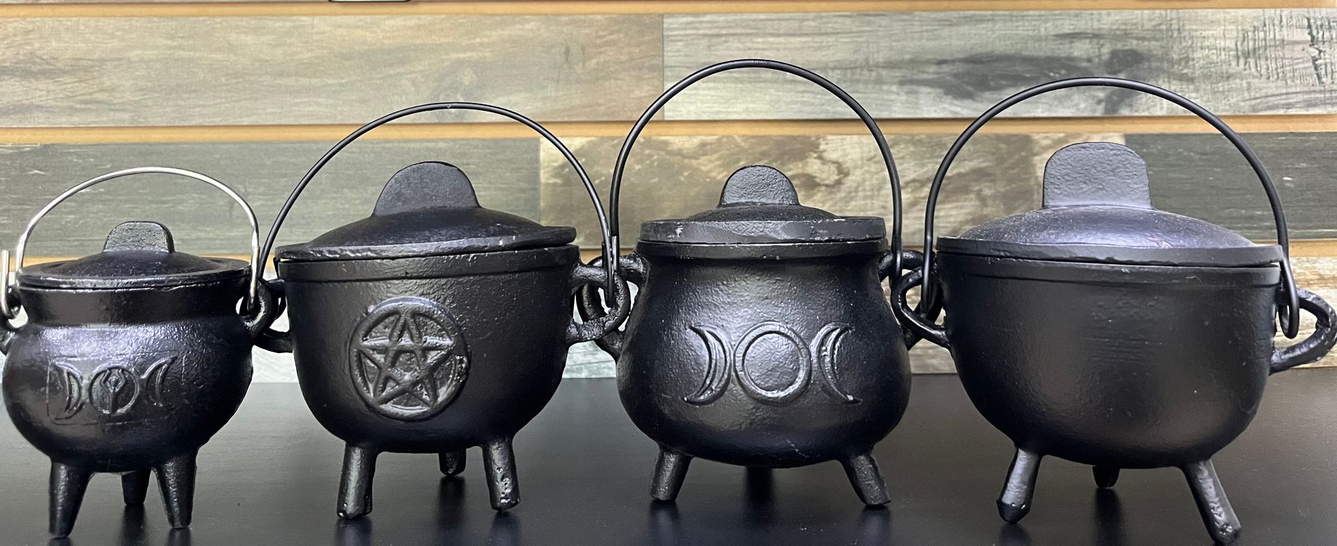 Four black cast iron cauldrons of increasing size, each with a lid, legs, and handle. 