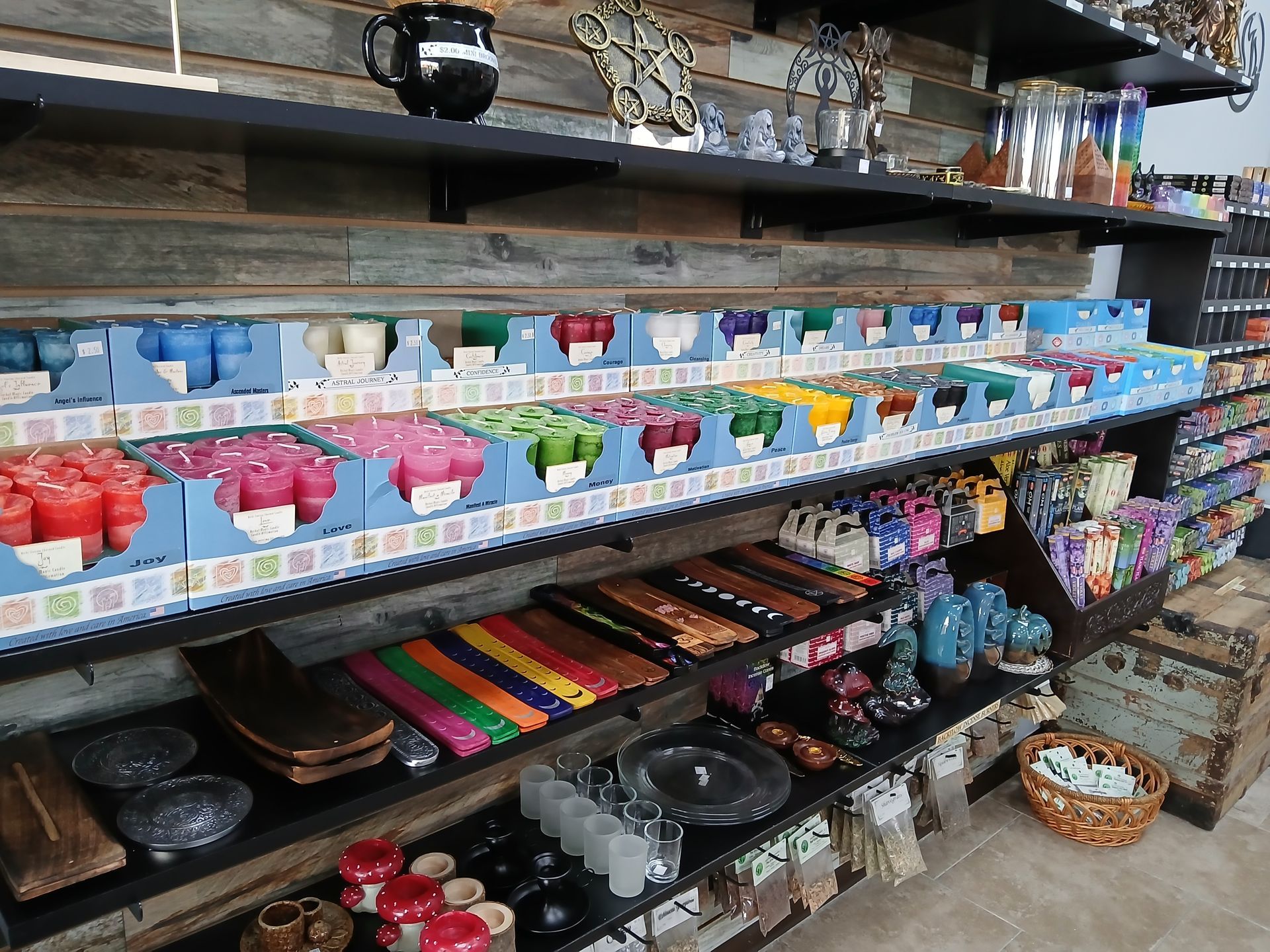 Shelves filled with colorful candles, decorative items, and a basket of stones inside a shop. 