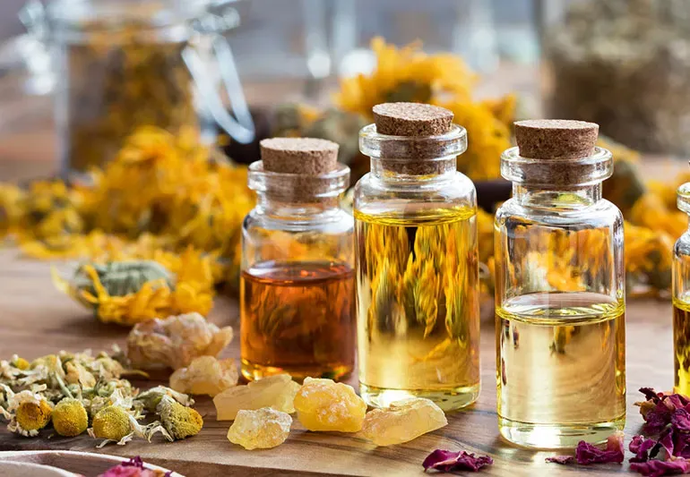 Bottles of essential oils with dried flowers, herbs, and amber resin, on a wooden surface.