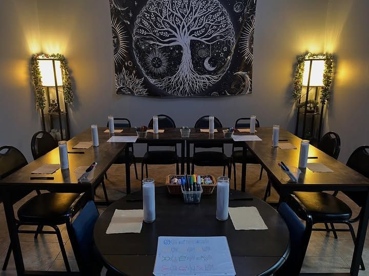 A warmly lit room with tables arranged for a gathering, under a tree of life tapestry.