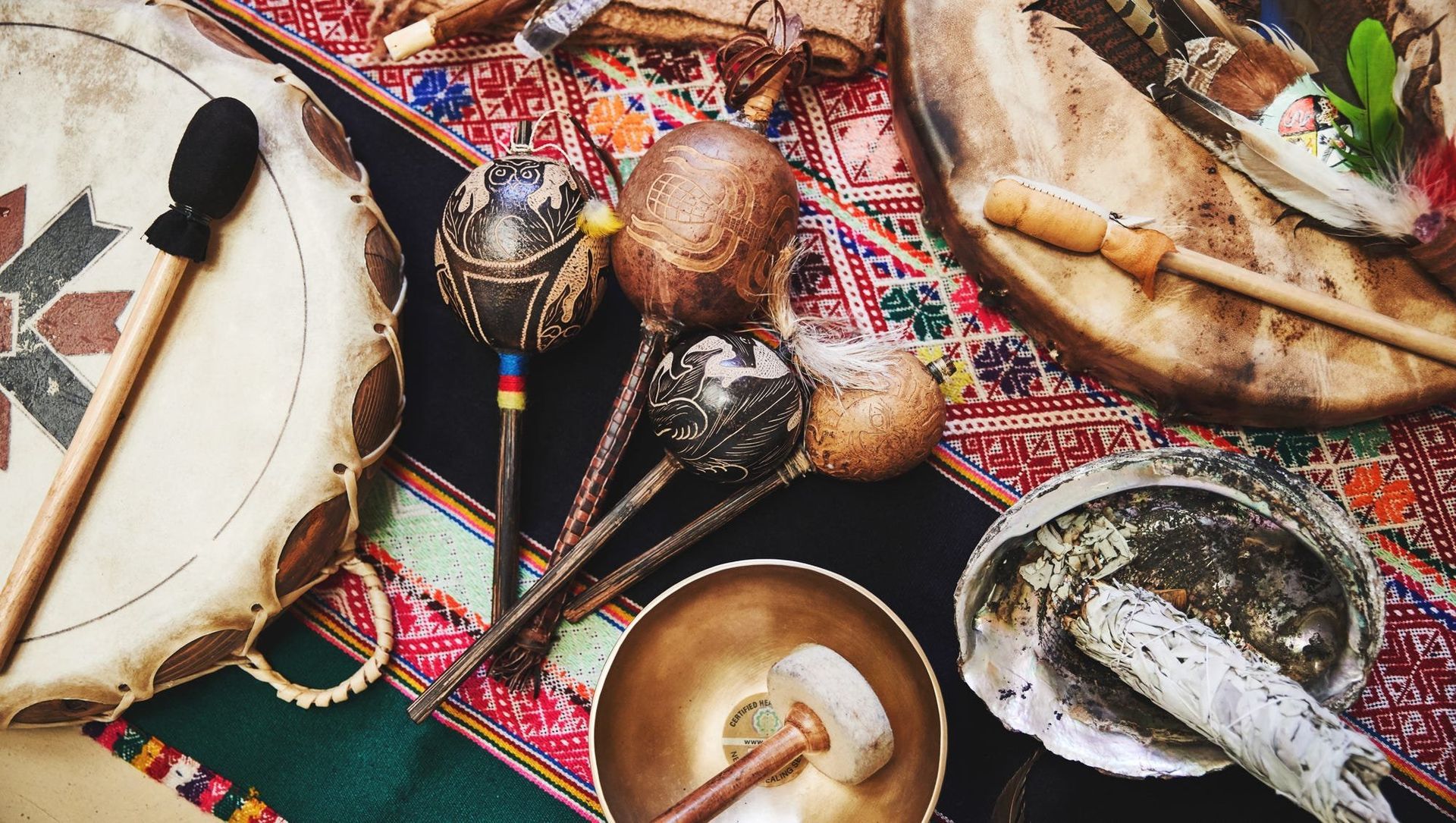 A collection of various percussion instruments on a patterned cloth, including drums, shakers, and a singing bowl.