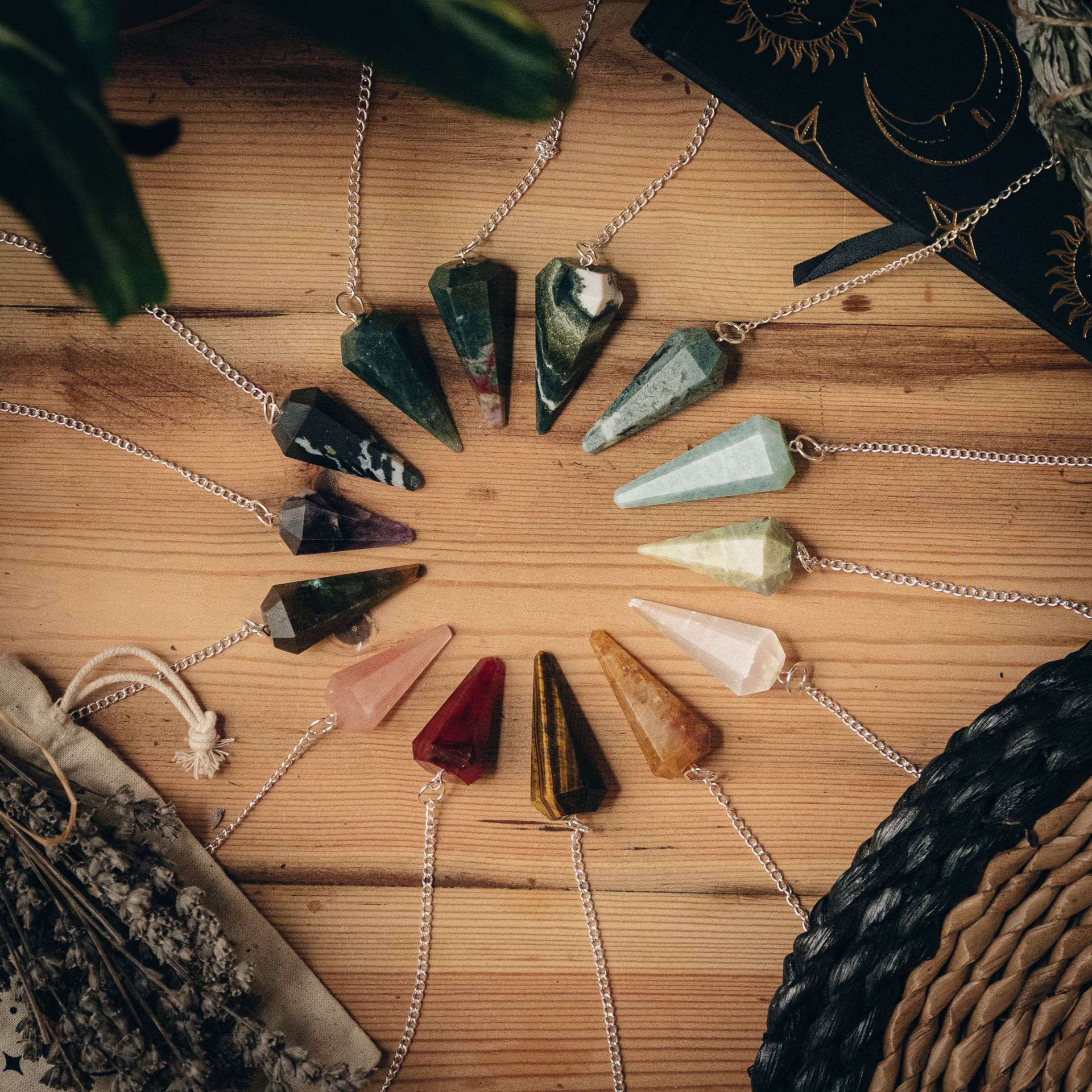 Collection of crystal pendulums arranged on a wooden surface. Various colors and shapes, with silver chains.