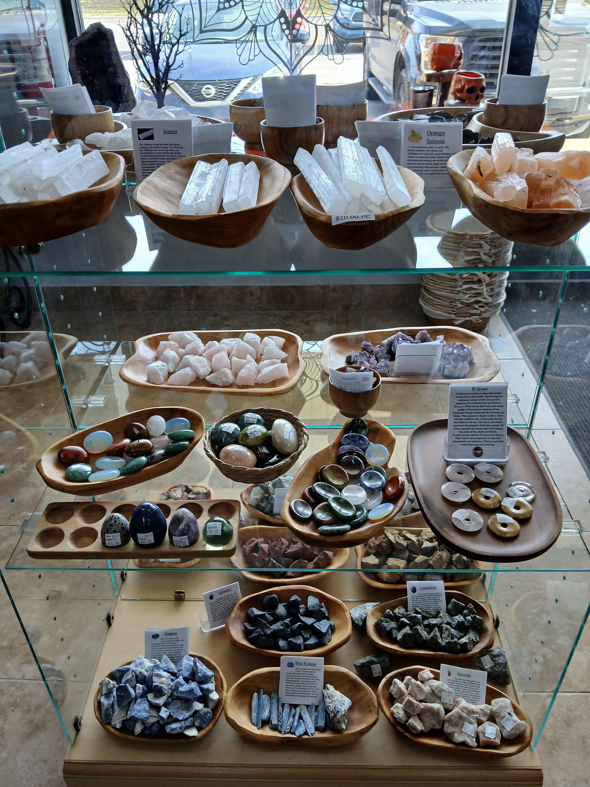 A glass display case filled with various polished crystals and gemstones arranged in wooden bowls, likely for sale in a shop.