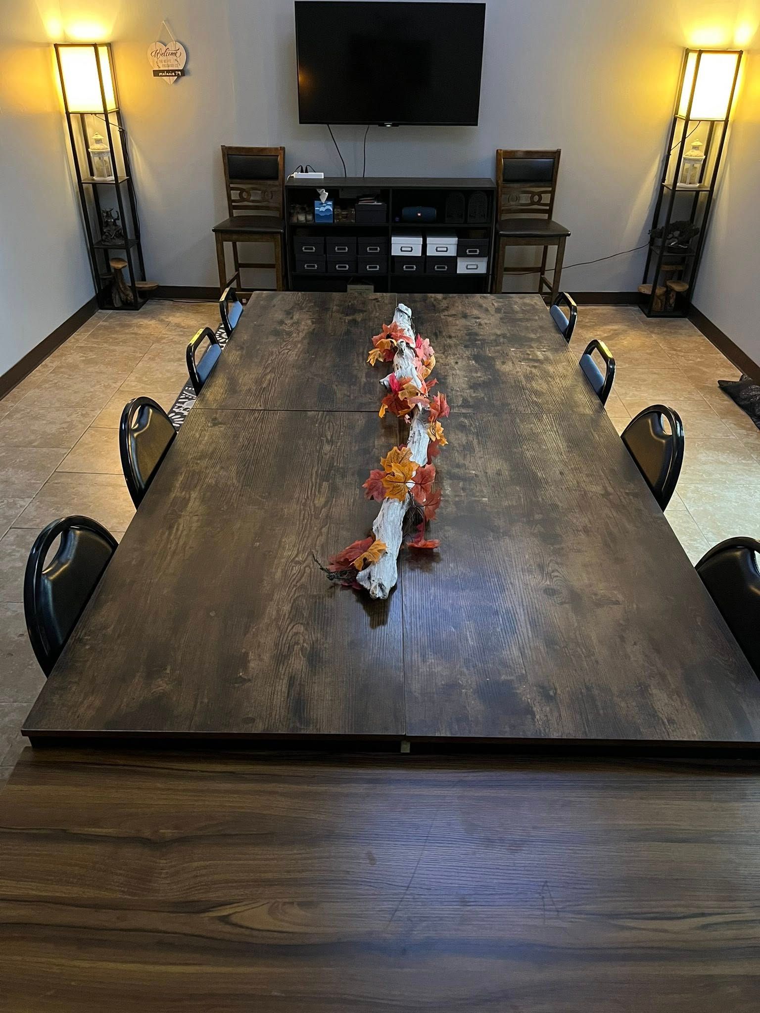 Long wooden table with fall centerpiece, set in a room with a TV and wall sconces.