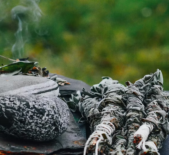 Sage bundle smoldering, releasing smoke. Green foliage in the background.