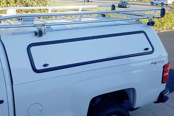 A white truck with a canopy on top of it is parked on the side of the road.