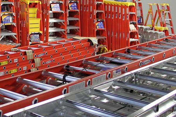A bunch of ladders are stacked on top of each other in a warehouse.